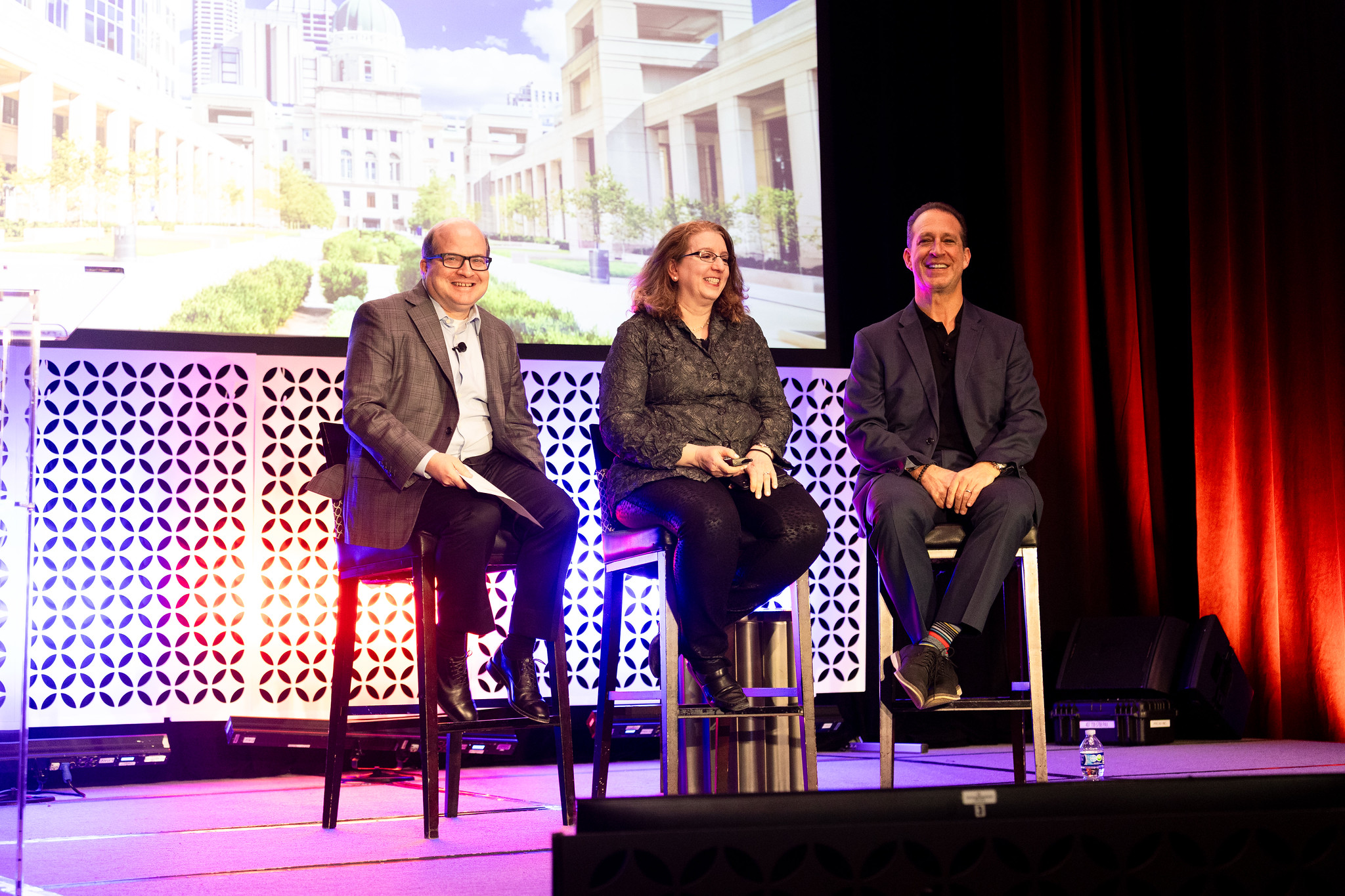 Two men and a woman sit on stools on the DEAMcon stage during their presentation.