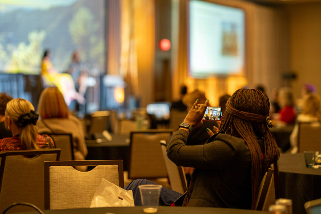 An attendee quickly snaps a photo of slides and presenter interaction.