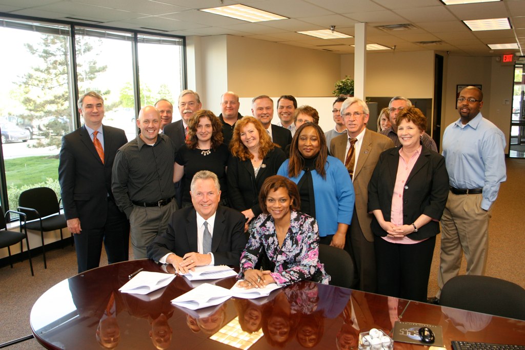 Bill Warren and a NASWA representative sign the 2010 National Labor Exchange partnership extension as staff from both organizations gather behind them.