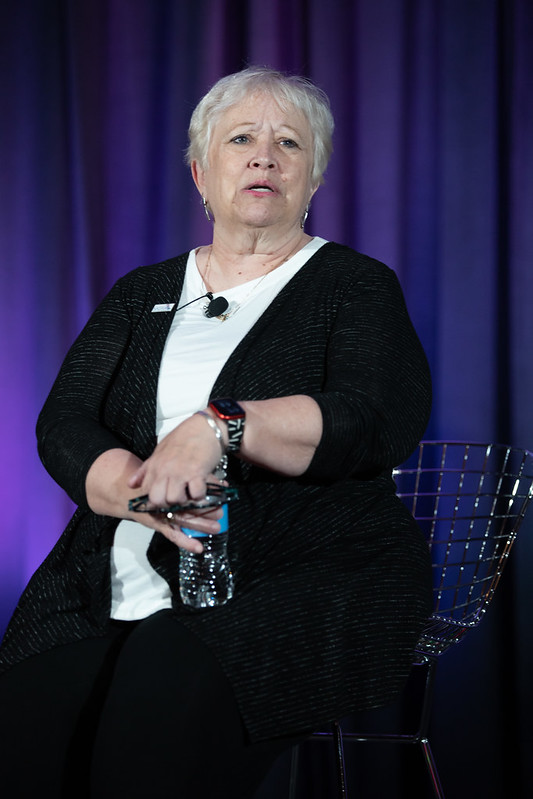 Lori Adams sits in chair holding water bottle during her on-stage presentation.