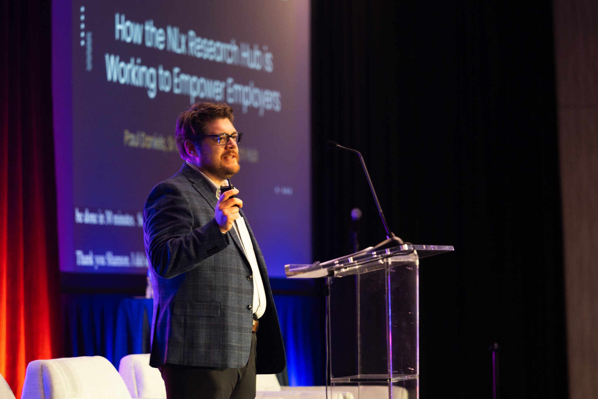 A man stands at a podium during his presentation on the DEAMcon stage.