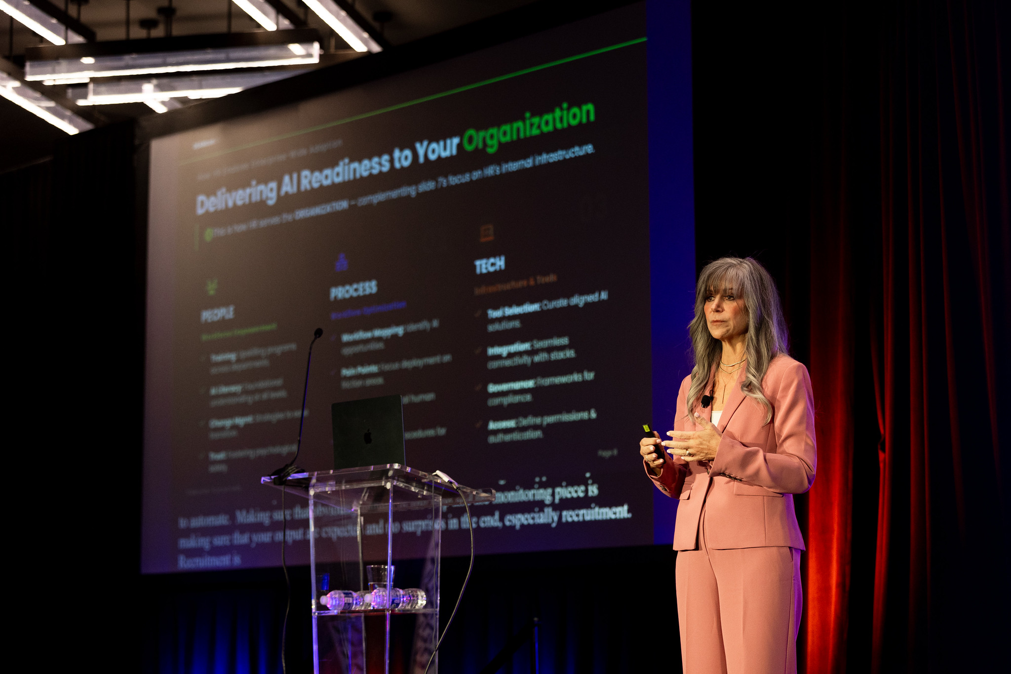 A woman presents on the DEAMcon stage with a presentation displayed on the screen behind her.