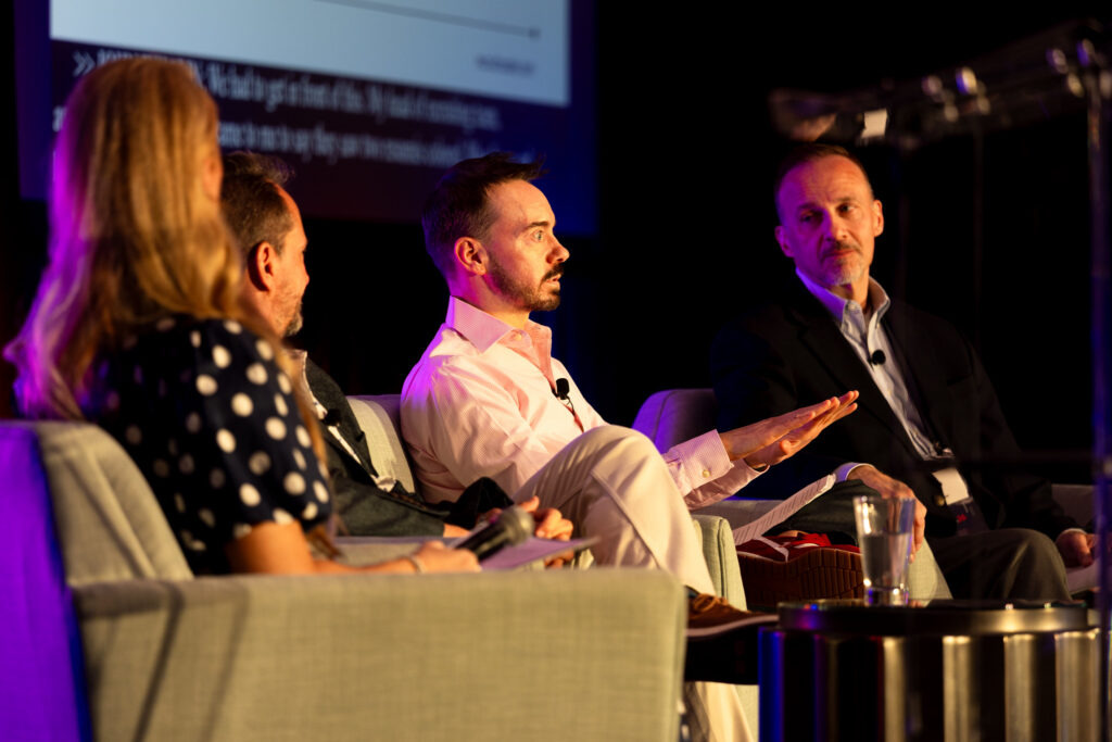 One woman and three men sit in chairs on the DEAMcon stage during their session.