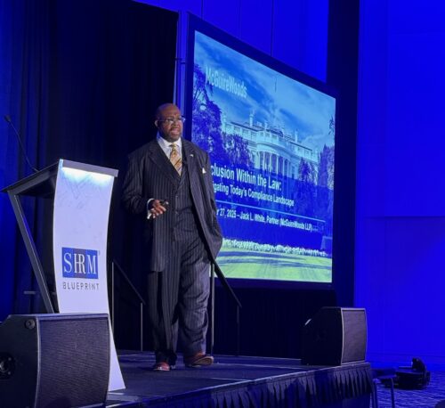 Speaker Jack White in pinstripe suit presenting at podium on stage with SHRM Blueprint branding and compliance law presentation slide