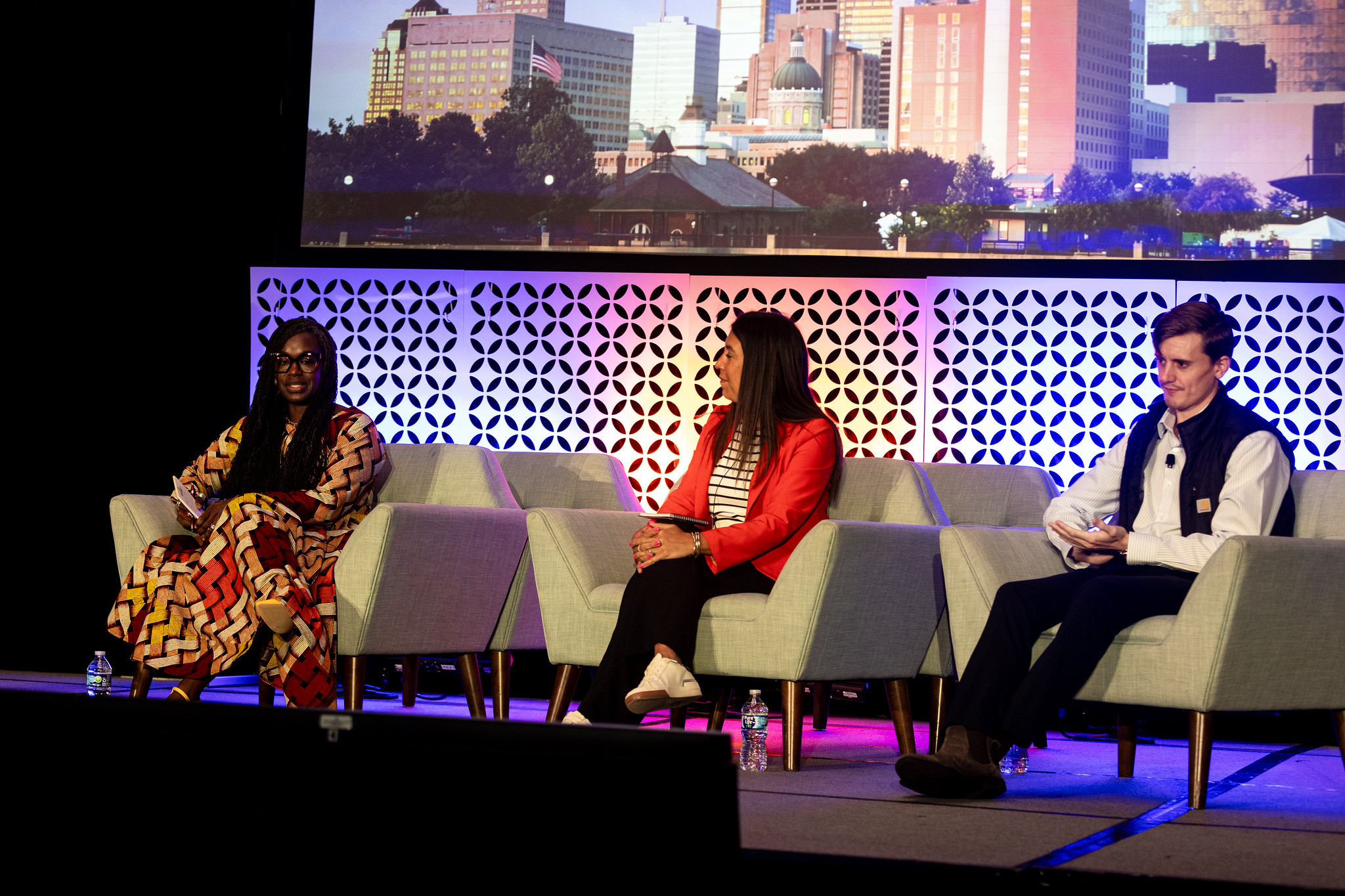 Two women and a man sit in chairs on the DEAMcon stage during their panel discussion.
