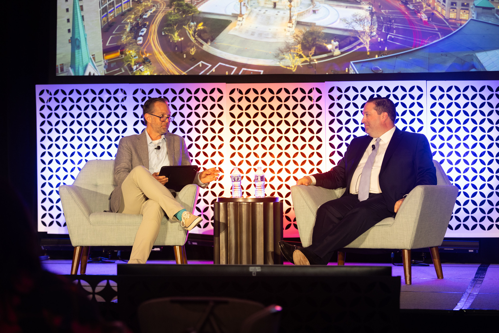 Two men sit in chairs on a stage during a fireside chat at DEAMcon26.