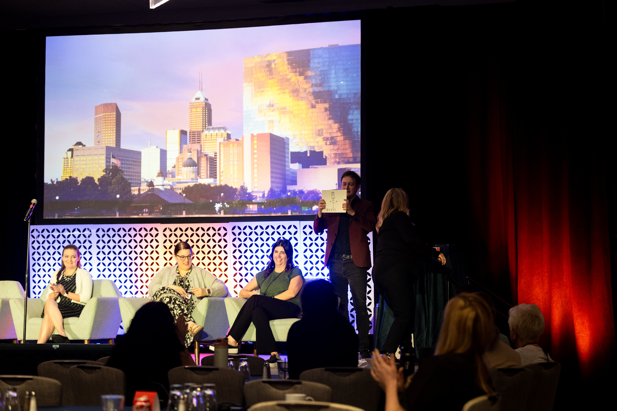 Participants sit in chairs on the DEAMcon stage while mentalist Christophe Fox holds up a hand-drawn picture.