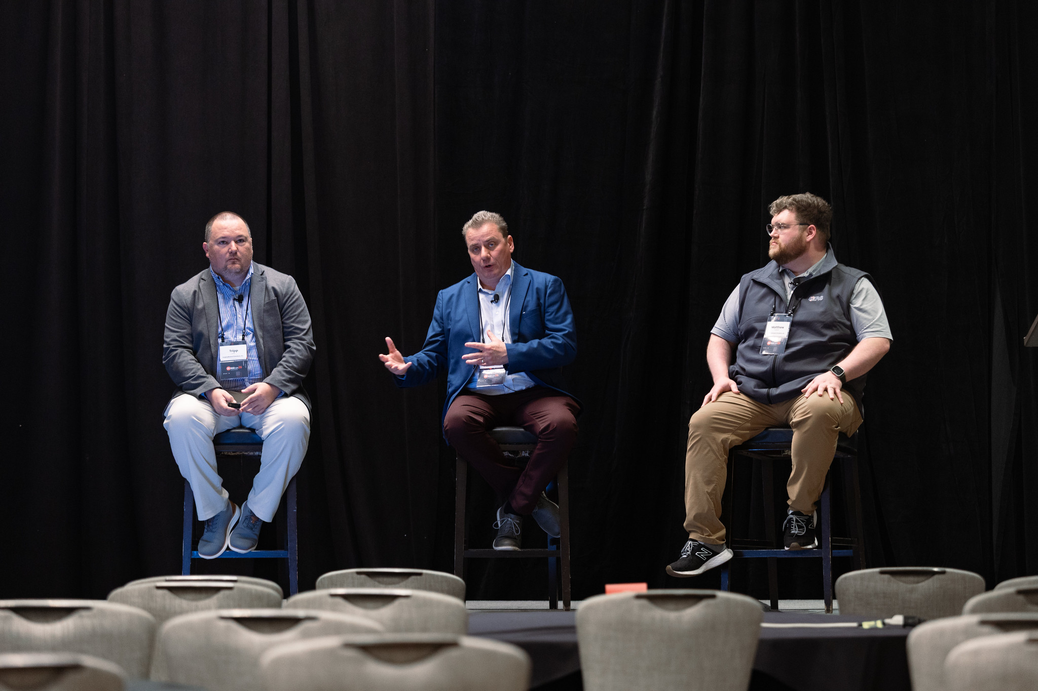 Three men sit on stools during their presentation at DEAMcon26.