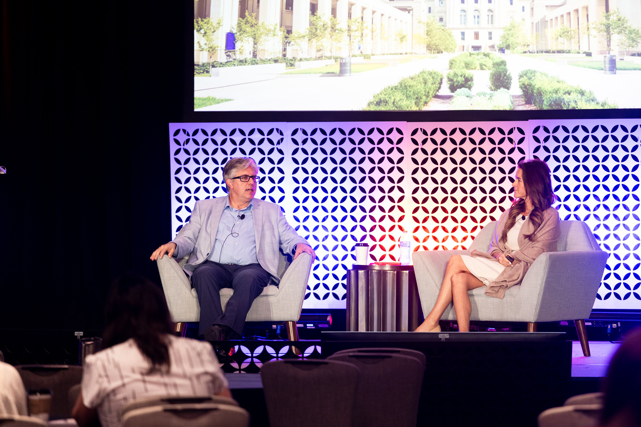 A man and woman sit in chairs on the DEAMcon stage during their presentation.