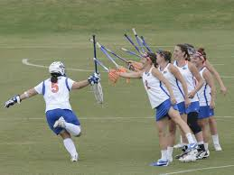 Women on a field in lacrosse gear tapping their lacrosse sticks in camaraderie