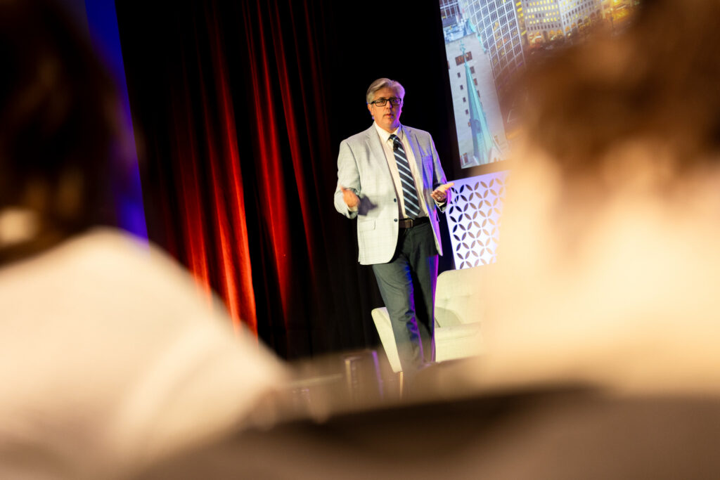 A man stands on the DEAMcon stage during his presentation