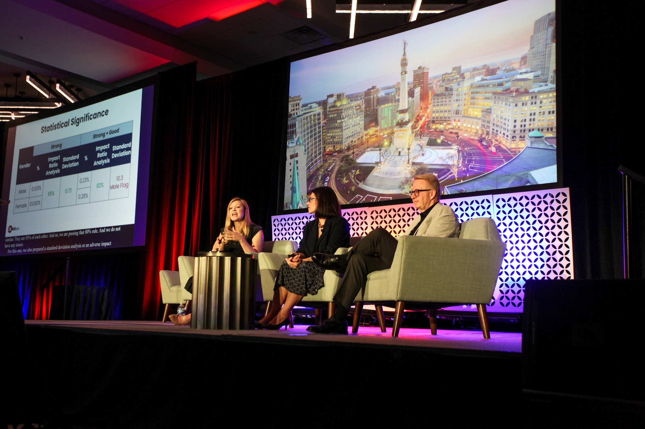 Two women and a man sit in chairs on the DEAMcon stage.