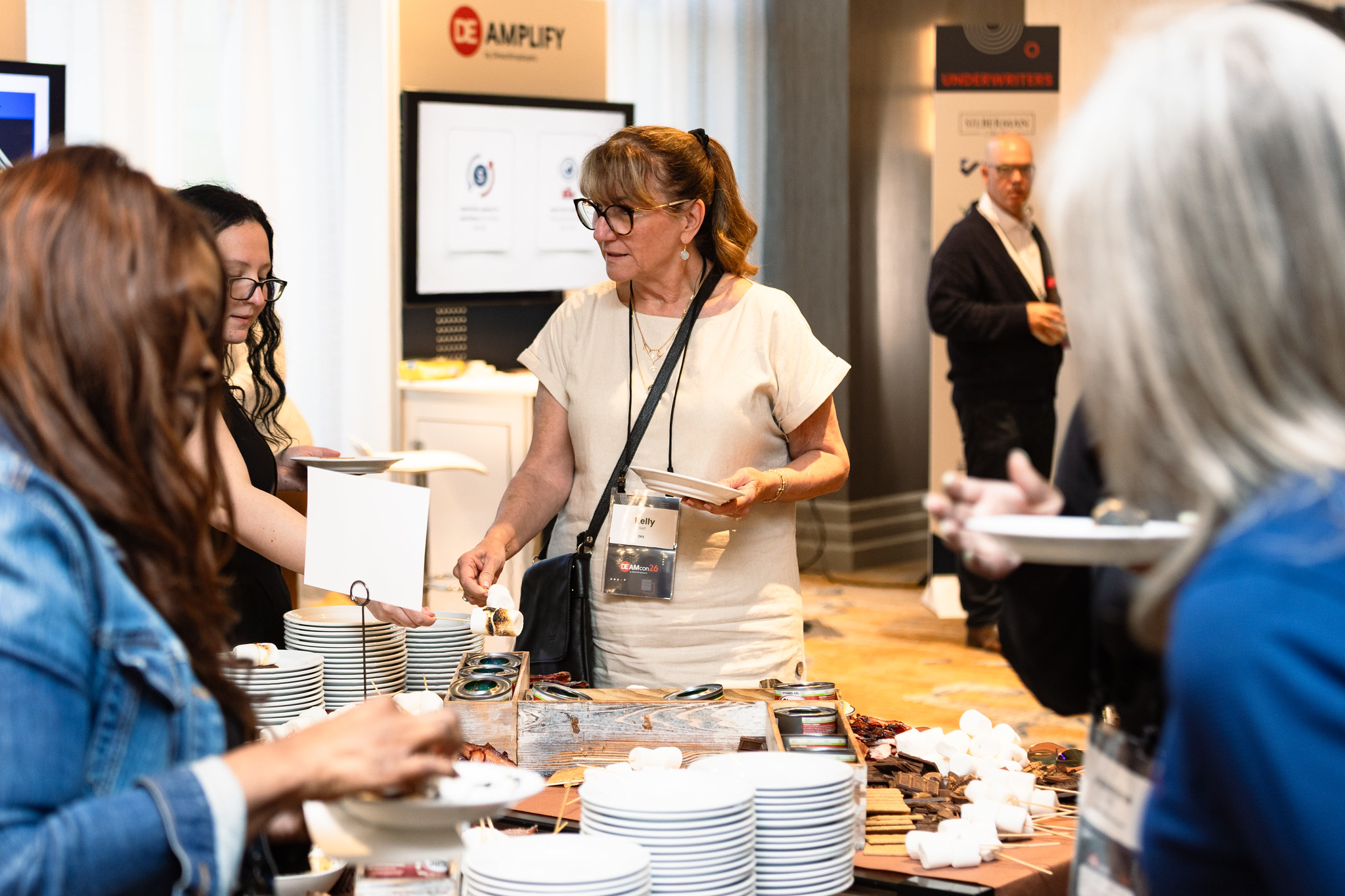 A group of women stand around a DIY s'mores station during a reception at DEAMcon26.